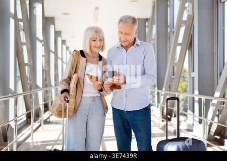 Mature couple standing in airport, man using smartphone while woman holds passport Stock Photo