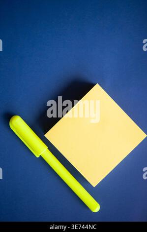 Minimal flat lay of yellow sticky note and neon marker on blue background with copy space for text Stock Photo