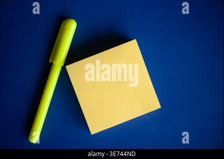 Minimal flat lay of yellow sticky note and neon marker on blue background with copy space for text Stock Photo