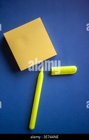 Minimal flat lay of yellow sticky note and neon marker on blue background with copy space for text Stock Photo