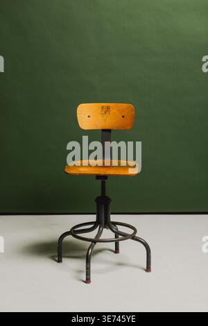 An empty vintage drafting stool against a green paper backdrop in a studio setting Stock Photo