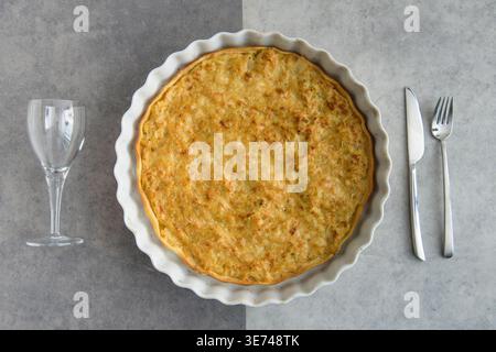 Quiche tarte served in a white baking dish with empty wine glass and cutlery Stock Photo