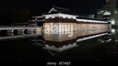 A traditional Japanese castle,in Hiroshima city, structure with stone walls and wooden accents is beautifully reflected in the still water at night, Stock Photo