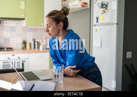 Interested smiling mature woman watching media online on laptop, looking through viral content. Stock Photo