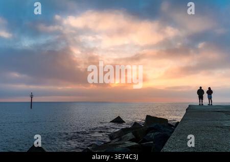 Romantic Couple Standing Together on Stone Pier at Sunrise Watching Mediterranean Sea Under Dramatic Cloudy Sky Stock Photo