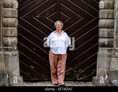 Elderly caucasian female in front of historic wooden door with stone pillars. Stock Photo