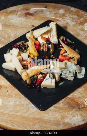 Gourmet cheese platter with assorted brie blue cheese and hard cheese served with fresh berries nuts and honey on a black slate board. Stock Photo
