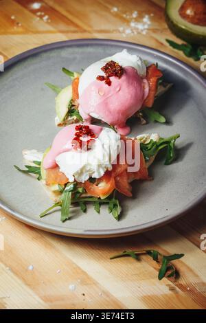 Gourmet Eggs Benedict with smoked salmon, avocado slices and vibrant pink beet hollandaise sauce served on a grey plate. Stock Photo