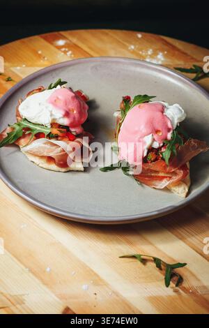 Gourmet poached eggs on prosciutto and flatbread with vibrant pink beet hollandaise sauce and fresh arugula. Stock Photo