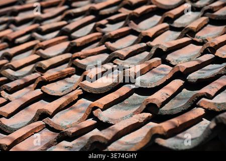 Red clay roof tiles texture. Close-up of an aged ceramic tiled roof. Old weathered terracotta roof tiles on a traditional house. Rustic architectural Stock Photo