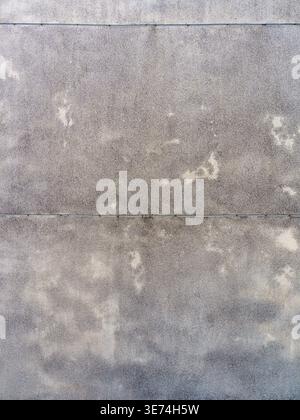 Close-up view of a flat, weathered grey concrete or stone wall surface showing abstract stains, discoloration, and rough textures under daylight. The Stock Photo