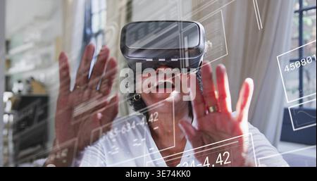Reaching senior woman wearing white blouse, hoop earrings using VR headset at home, translucent UI. Elder, technology, immersive, interaction, livingr Stock Photo