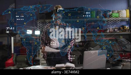 Reviewing docs, female tech in plaid, dark pants checking laptop on garage bench, hologram overlay. Automotive, diagnostics, engineer, workshop, data, Stock Photo