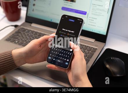 Kyiv, Ukraine. February 19, 2026. Woman using ChatGPT mobile app on a smartphone at a desk with a laptop. Artificial intelligence and remote work. Stock Photo