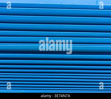 A detailed close-up showing the horizontal lines of a bright blue closed metal roller shutter door under daylight. The image illustrates commercial se Stock Photo