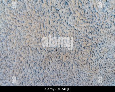 A detailed macro shot of a rough, bumpy grey stucco or roughcast plaster surface. This image serves as an ideal background plate representing construc Stock Photo