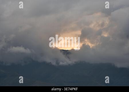 Dark Clouds With Sunlight Breaking. Intense Weather And Lightning Illuminating Rugged Mountain Landscape Stock Photo