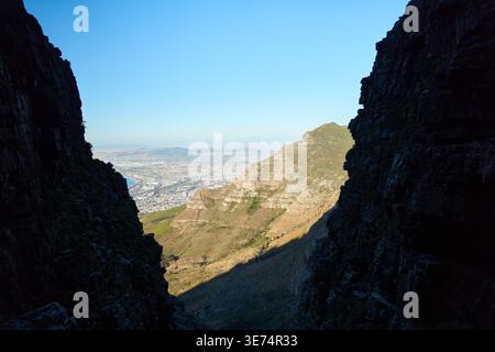 Mountain Pass Vista. Scenic View Of City And Ocean. Sunlit Mountain Gorge With City In Distance Stock Photo
