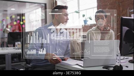 Reviewing pair in blue shirt and beige blazer discussing laptop with AR overlay, papers at office. Collaboration, data, visualization, dashboard, moni Stock Photo