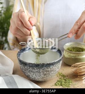 Woman sifting matcha powder into bowl at wooden table, closeup Stock Photo