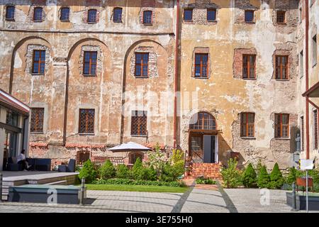 A weathered historic building facade with peeling plaster revealing underlying brickwork, featuring multiple arched and rectangular wooden-framed Stock Photo