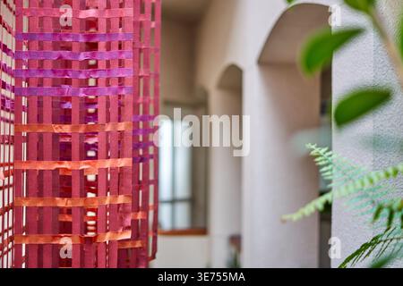 Close-up view of a colorful woven textile installation composed of intersecting fabric strips in shades of red, purple, pink, and orange, creating a Stock Photo