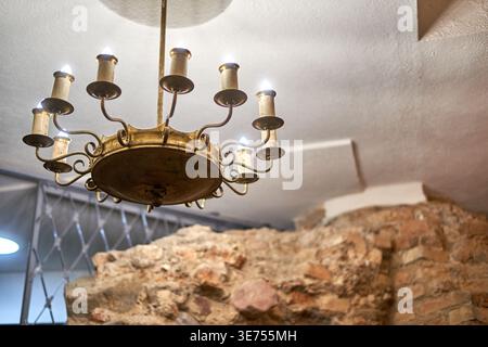 A vintage brass chandelier with multiple candle-style electric lights hangs from a white ceiling. The ornate lighting fixture features curved arms Stock Photo