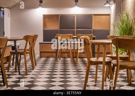 Interior view of a modern, empty cafeteria or casual dining area featuring a distinctive black and white checkered floor pattern. The space is Stock Photo
