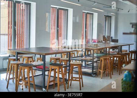 A bright, modern interior space featuring multiple large standing-height tables with dark wooden tops and metal frames on wheels, surrounded by Stock Photo