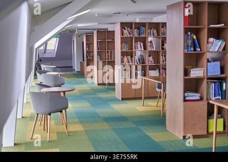 A modern library or study room interior featuring wooden bookshelves filled with books, contemporary gray upholstered chairs with wooden legs, and Stock Photo