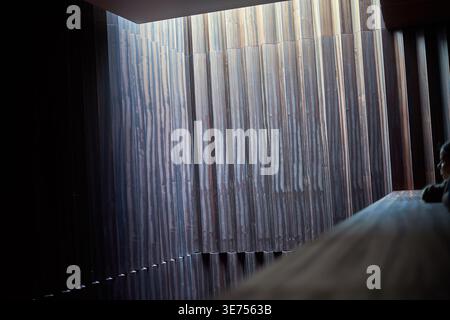 A contemporary architectural interior featuring a dramatic wall of vertically striated marble or stone panels with varying heights creating an Stock Photo
