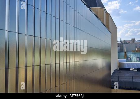 A close-up view of a modern building facade featuring vertical metallic panels with an iridescent, reflective surface displaying gradients of blue, Stock Photo