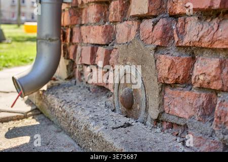 Close-up view of a weathered red brick building exterior wall featuring a circular rusty metal anchor plate with central bolt embedded in the masonry Stock Photo