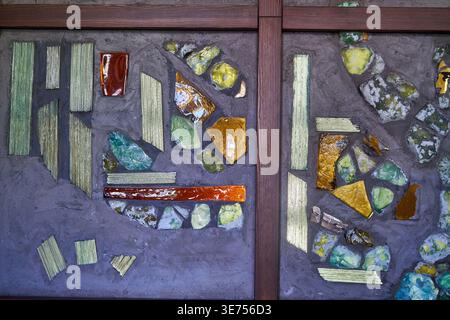 Abstract mosaic artwork featuring irregular fragments of colored glass and ceramic pieces in shades of green, amber, orange, and red, embedded in a Stock Photo