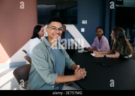 Smiling young businessman with diverse coworkers during meeting in boardroom at office during daytime Stock Photo