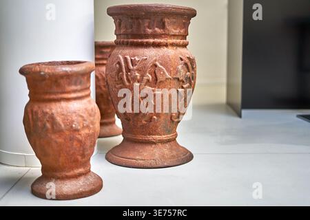 Three antique terracotta urns or vases with ornate decorative patterns displayed on a light-colored tiled floor indoors. The vessels feature a Stock Photo