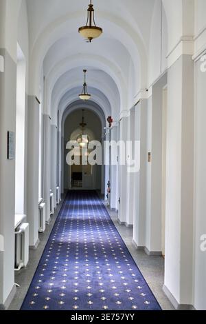 A long, empty corridor in a historic or institutional building features white walls and a series of elegant arched ceilings receding into the Stock Photo