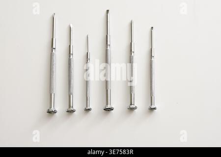 Top view of a set of small screwdrivers arranged in a row on a clean white table. Minimalist industrial composition with studio lighting Stock Photo