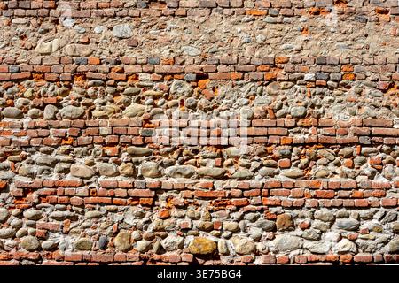 Horizontal-course masonry alternating rows of solid clay bricks with layers of river pebbles or stones, Old full-frame texture wall Stock Photo
