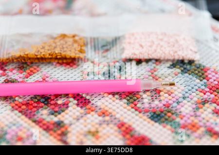 Colorful beads and a pink pen on a floral patterned fabric. The scene showcases crafting materials for projects and creative hobbies Stock Photo
