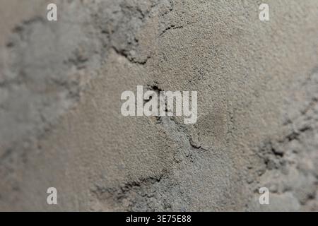 Close-up of textured gray plaster wall with visible cracks and uneven surface. Material appears rough and weathered, showcasing a natural, industrial Stock Photo