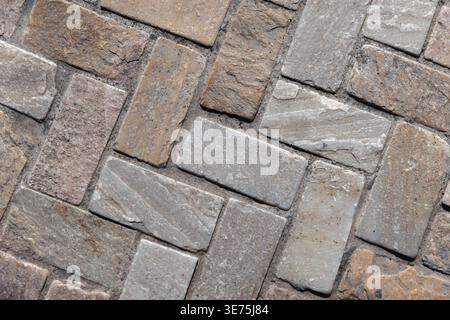 Close-up of textured stone pavers arranged in a herringbone pattern, showing natural color variations, rough surfaces and mortar joints. Background ph Stock Photo