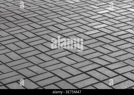 Perspective view of concrete pavers arranged in a geometric pattern, with repeating lines, gritty texture and shadowed contrast in monochrome urban pa Stock Photo