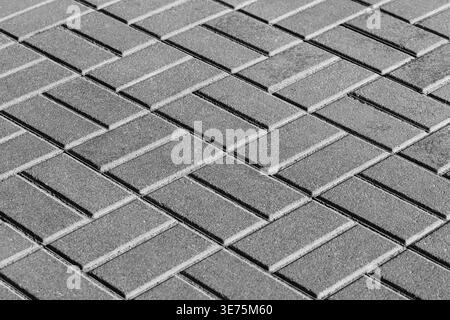 Close-up view of concrete pavers arranged in a geometric pattern, showing repeating lines, gritty texture and shadowed contrast in monochrome urban pa Stock Photo