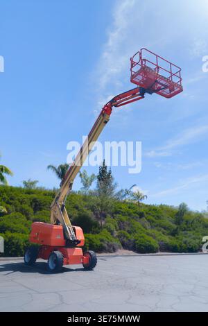 A telescopic boom lift extends high into the air with an empty safety basket positioned against a bright blue sky. The industrial equipment stands on Stock Photo