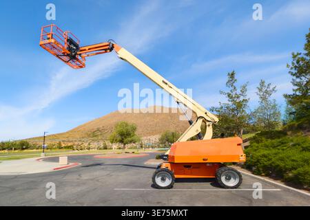 A telescopic boom lift extends high into the air with an empty safety basket positioned against a bright blue sky. The industrial equipment stands on Stock Photo