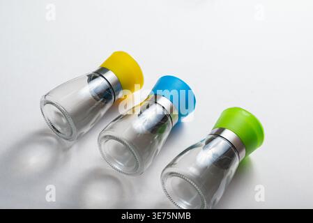 Three salt shakers. Soft studio lighting showcases glass texture. Yellow, blue, green plastic lids, set against a white backdrop. Clean, minimalist co Stock Photo