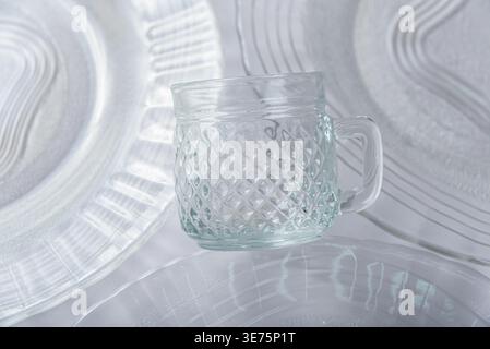 Studio shot features clear glass mug with textured diamond pattern, resting softly on similarly styled transparent plates. Subtle shadows, monochromat Stock Photo