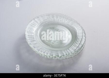 Stack of clear glass plates, isolated on white. Minimalist and clean setup, diffused lighting highlighting textures. Ideal for showcasing kitchenware, Stock Photo