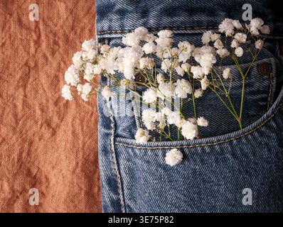 Delicate white flowers arranged in denim pocket over rustic linen background creating soft feminine western aesthetic perfect for country bridal Stock Photo
